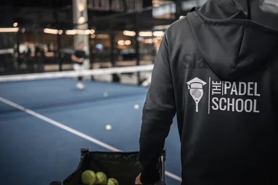 A coach from The Padel School wheeling a basket of balls onto an indoor padel court