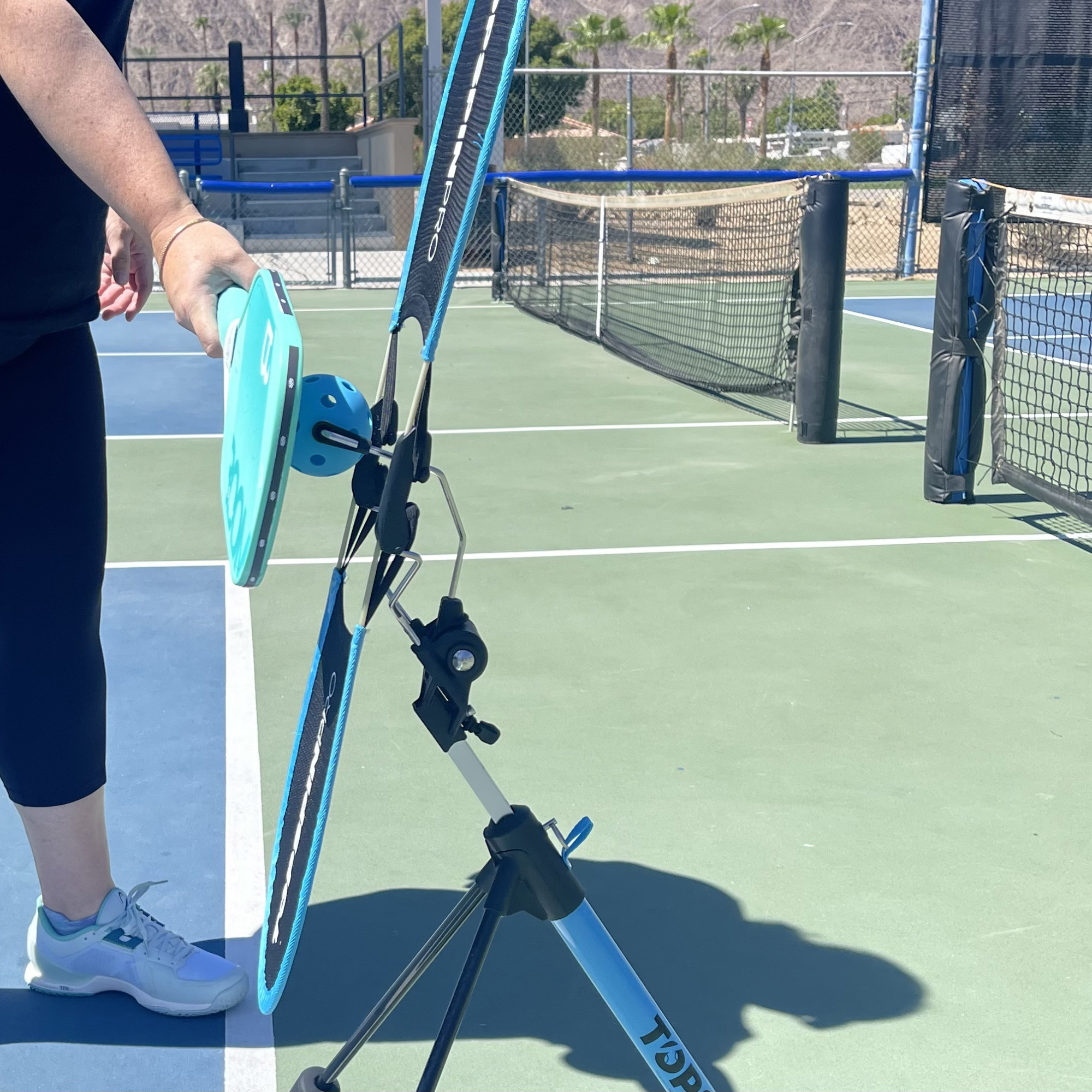 Player brushing up on a pickleball with the TopspinPro Pickleball, side view on an outdoor court